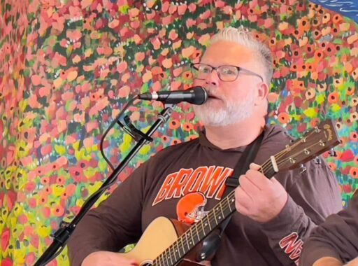 Michael Crawley, white-haired, performing guitar and singing